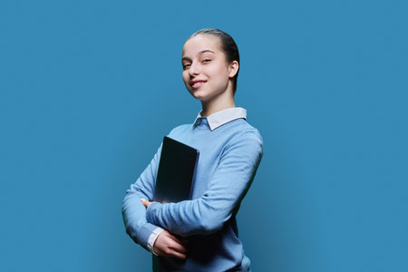 Portrait of teenage high school student girl with laptop in hands on blue backgroundの写真素材