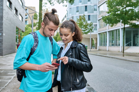 Teenage friends guy and girl standing together using smartphonesの写真素材