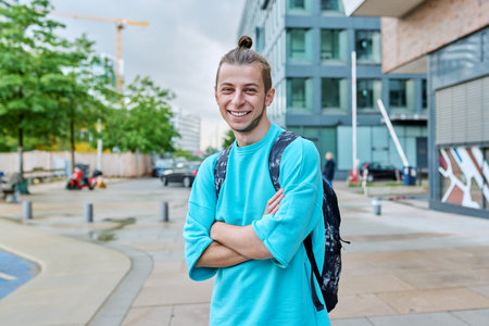 Happy young guy with backpack with crossed arms outdoor, city background