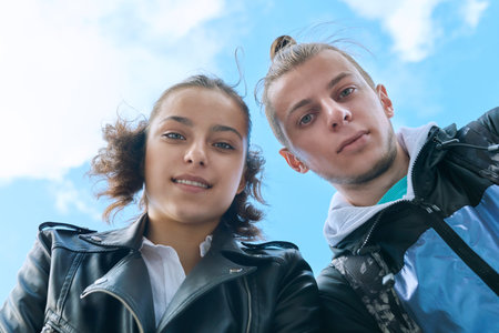 Teenage guy and girl smiling looking down at camera, blue sky background