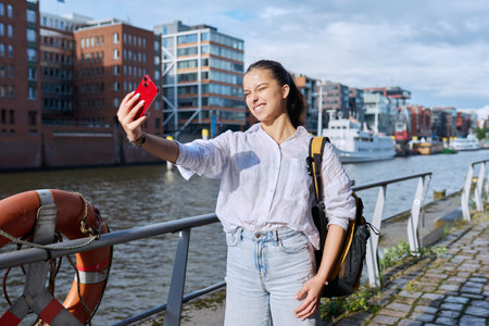 Young teenage female student tourist taking selfie photo on smartphone in European port cityの写真素材