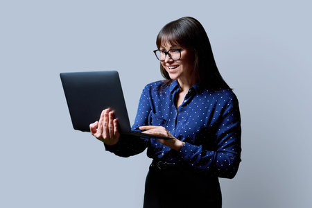 Smiling business middle aged woman using laptop on gray backgroundの写真素材