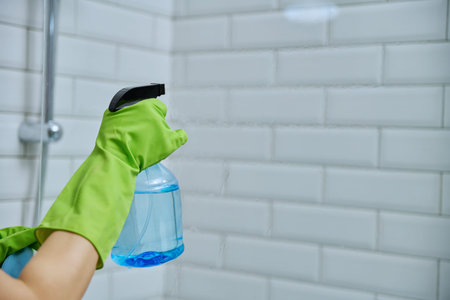 Close-up hands in gloves cleaning bathroom, washing glass in shower