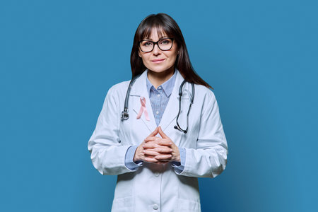 Portrait of female doctor in white coat with pink ribbon on blue backgroundの写真素材