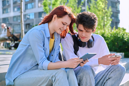 Teenage youth guy and girl college students sitting outdoor using smartphoneの写真素材