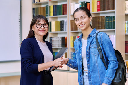 Female teacher shaking hands to teenage girl high school student, inside educational buildingの写真素材