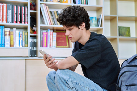 Relaxed young male college student using smartphone, sitting inside classroomの写真素材