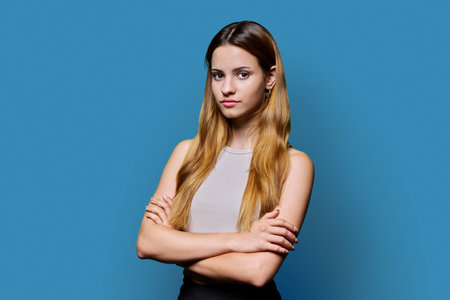 Beautiful young girl with crossed arms looking at camera on blue backgroundの写真素材