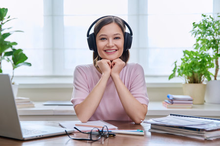 Portrait of young female student wearing headphones, sitting at home at deskの写真素材