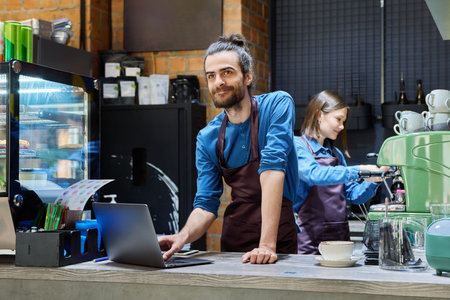 Two cafe workers working together behind counter, at coffee shop