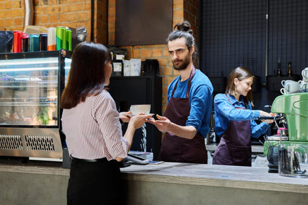 Guy working in cafe with cup of coffee at bar counter serving female clientの写真素材
