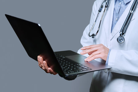 Close-up of female doctor hands using laptop on grey studio backgroundの写真素材