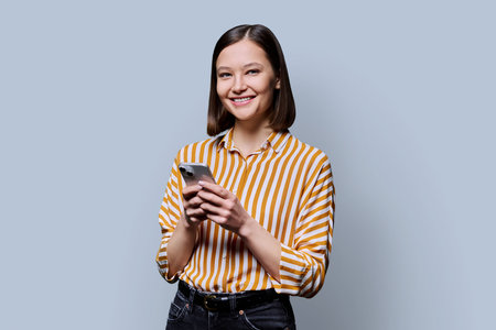Young smiling woman using smartphone looking at camera in grey backgroundの写真素材