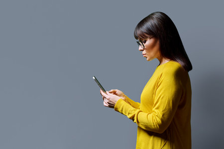 Profile view middle aged woman using smartphone on grey backgroundの写真素材