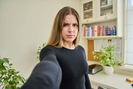 Close-up selfie portrait of teenage confused female looking at web camera