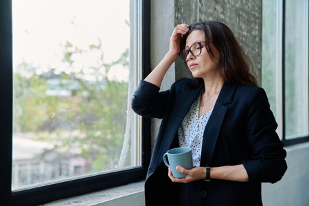 Mature tired, stressed businesswoman standing near windowの写真素材