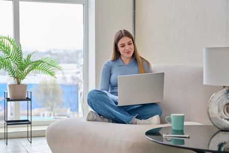 Portrait of young woman sitting in chair with laptop, in home interiorの写真素材