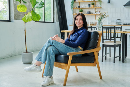 Portrait of beautiful 30s smiling woman sitting in armchair at home in living roomの写真素材