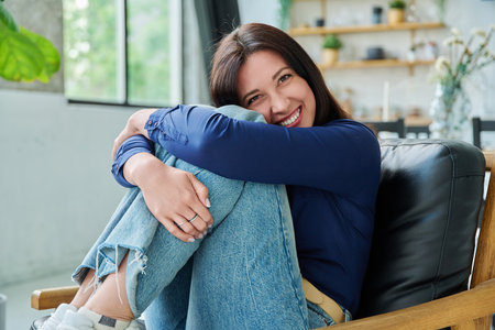 Portrait of beautiful young brunette woman sitting on chair in living roomの写真素材
