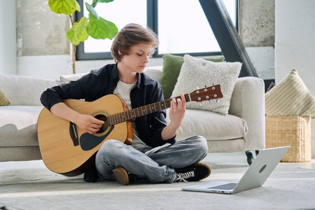 Teenage boy with acoustic guitar and laptop, having online music lessonの写真素材