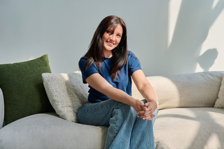Portrait of beautiful young brunette woman sitting on sofa in living roomの写真素材