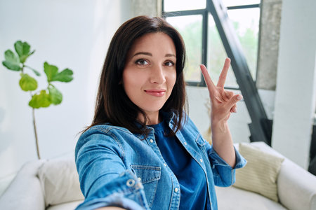 Selfie portrait happy beautiful woman making gesture victory success in homeの写真素材
