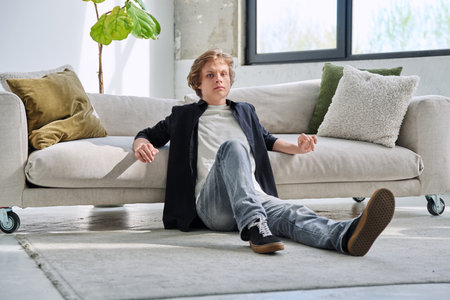 Portrait of handsome relaxed teenage boy sitting on floor near sofa in living roomの写真素材