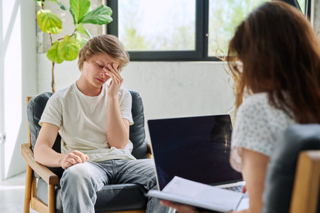 Sad teenage boy in mental therapy session, talking with behavioral psychologistの写真素材