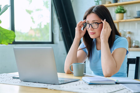 Young serious woman working with laptop sitting at table at homeの写真素材