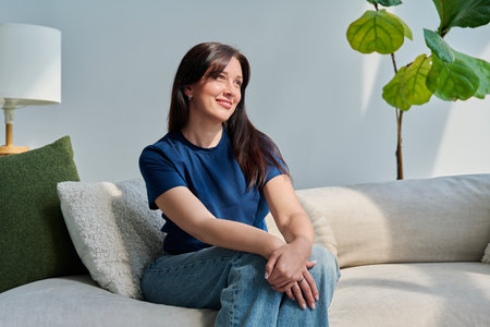 Portrait of beautiful young brunette woman sitting on sofa in living roomの写真素材