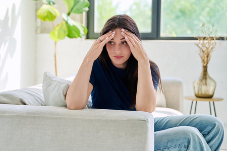 Sad upset young woman sitting on sofa at homeの写真素材