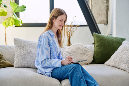Young woman using digital tablet sitting on sofa at homeの写真素材