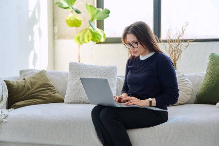 Portrait of middle aged woman using laptop sitting on sofa at homeの写真素材