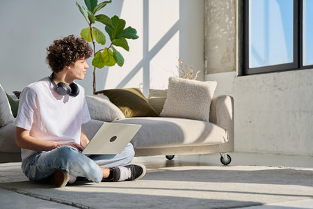Handsome young male typing on laptop sitting on floor at homeの写真素材