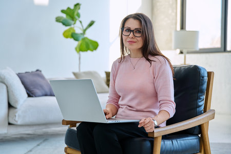 Middle aged business woman sitting in chair with laptop computerの写真素材