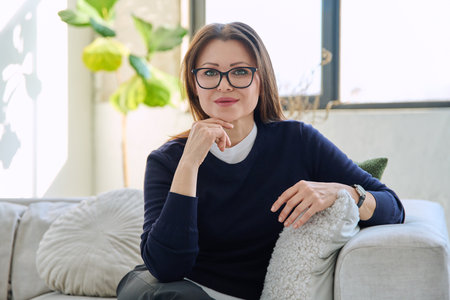 Portrait of beautiful middle aged smiling woman sitting at home on sofaの写真素材