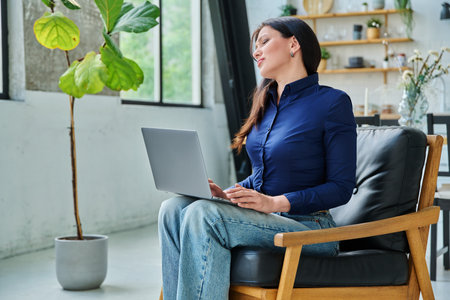 Tired woman working with laptop, having neck pain, sitting in chair with computerの写真素材