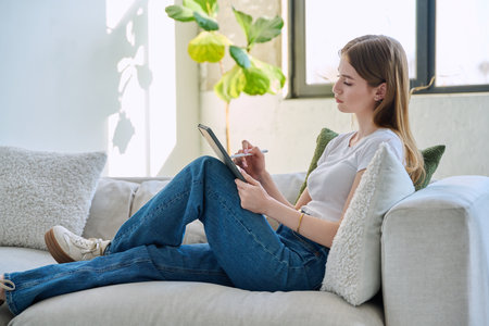 Young woman using digital tablet sitting on sofa at homeの写真素材