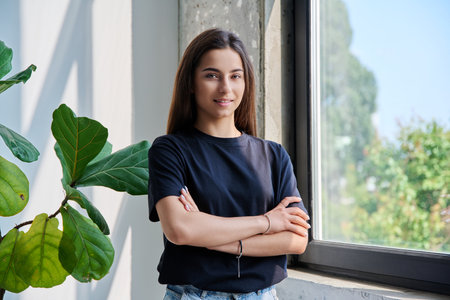 Portrait of confident successful teenage girl posing with crossed arms near windowの写真素材