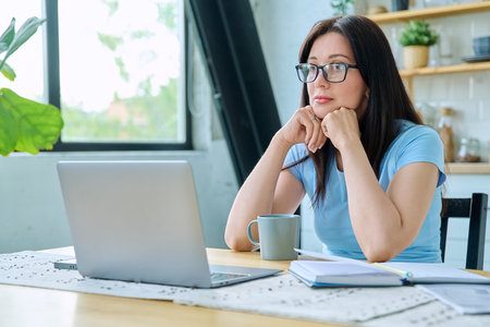 Young serious woman working with laptop sitting at table at homeの写真素材