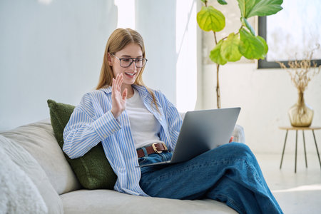 Young teenage girl using laptop for video chat sitting on sofa at homeの写真素材