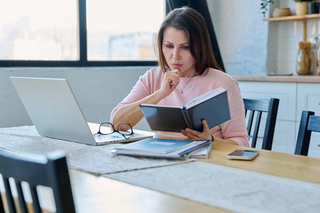 Middle-aged serious woman working at computer laptop in home officeの写真素材