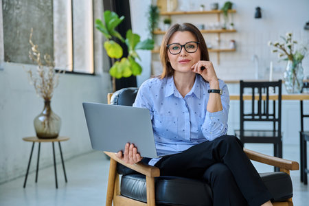 Middle aged business woman sitting in chair with laptop computerの写真素材