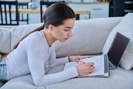 Young student girl study online, lying at home on couch with laptop, notebookの写真素材
