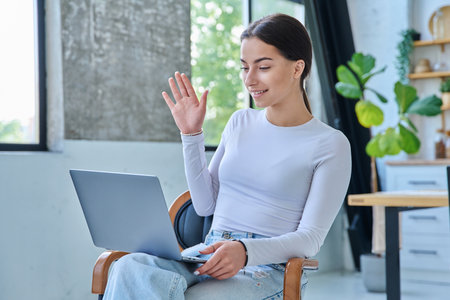 Young teenage girl using laptop for video chat sitting on chair at homeの写真素材
