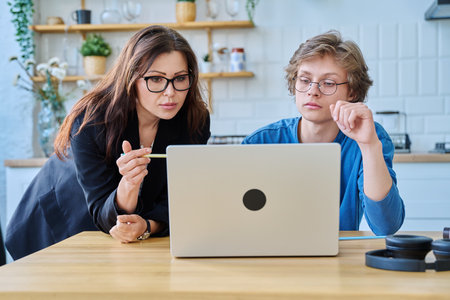 Teenage boy student with female mentor trainer teacher looking at laptop computer screenの写真素材