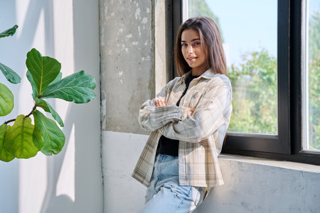 Portrait of confident successful teenage girl posing with crossed arms near windowの写真素材