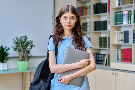 Portrait of teenage beautiful girl high school student posing in library classroom