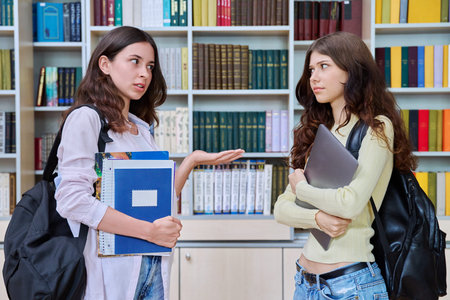 Two teenage students classmates chatting standing in classroom library