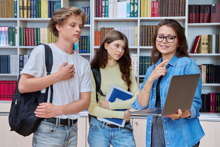 Two teenage students meeting talking with female teacher in libraryの写真素材